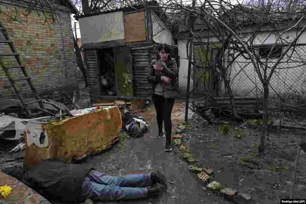 Ірина Гаврилюк з котом на руках проходить повз тіла свого чоловіка та брата. Буча, Фото від 4 квітня 2022 року.  Українські слідчі встановили, що під час російської окупації Бучі загинули понад 1400 людей, із них 37 дітей