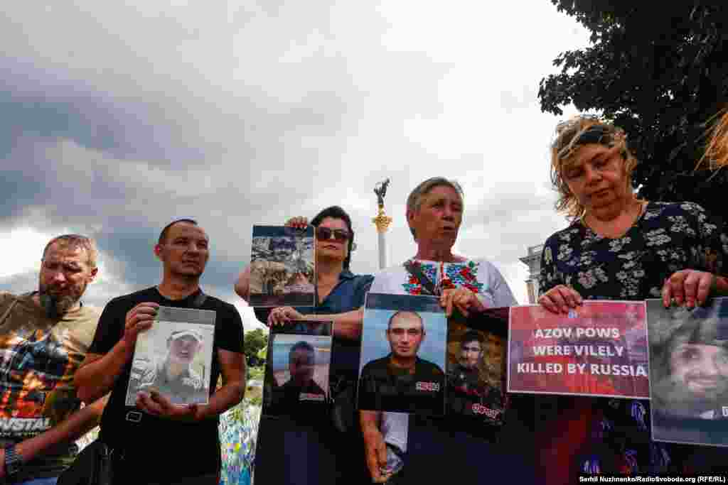 Поруч із фотографією військового жінка тримає плакат із написом: «Полонені азовці були підступно вбиті Росією» (переклад з англійської)