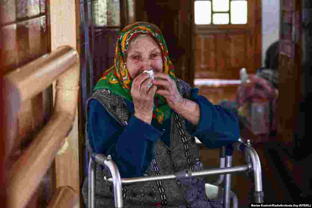 An elderly woman cries before her evacuation from the city. "What are they doing?" she asks, as the sounds of artillery are heard in the distance.