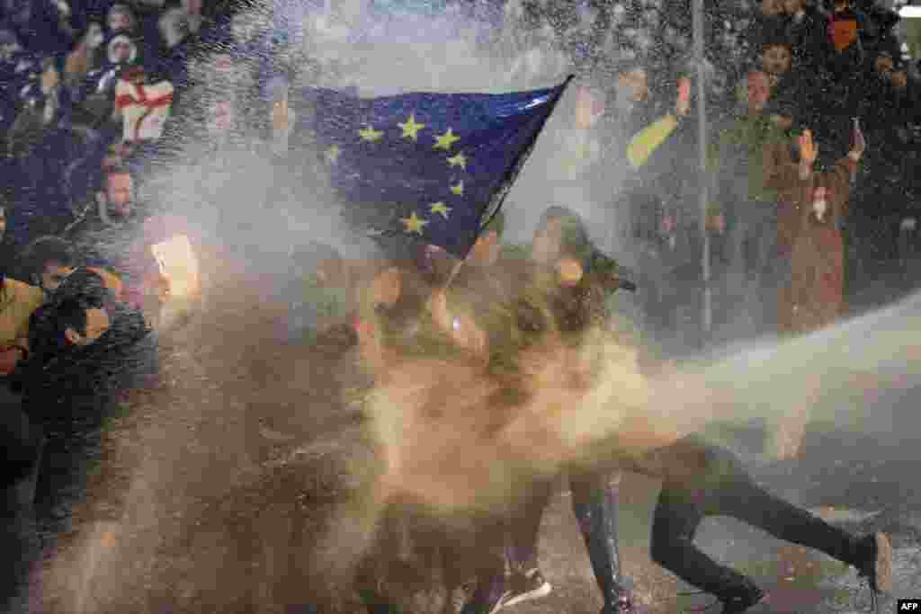 Протестующие, размахивающие флагом Европейского Союза, под огнем водометов во время столкновений с полицией возле парламента Грузии в Тбилиси, 7 марта 2023 года. Грузинская полиция применила слезоточивый газ и водометы против протестующих. Люди выступали против спорного законопроекта об "иностранных агентах". (Photo by AFP)