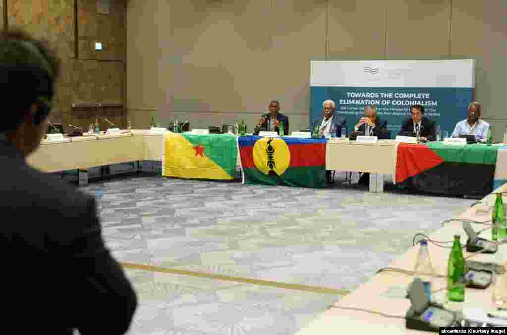 Azerbaijani flags began appearing in New Caledonia soon after political activists from several French territories were flown to Baku for a conference, called Towards The Complete Elimination Of Colonialism, in July 2023.  In this photo from the event, speakers sit behind flags used in the French territories of (left to right) French Guiana, New Caledonia, and Martinique.   
