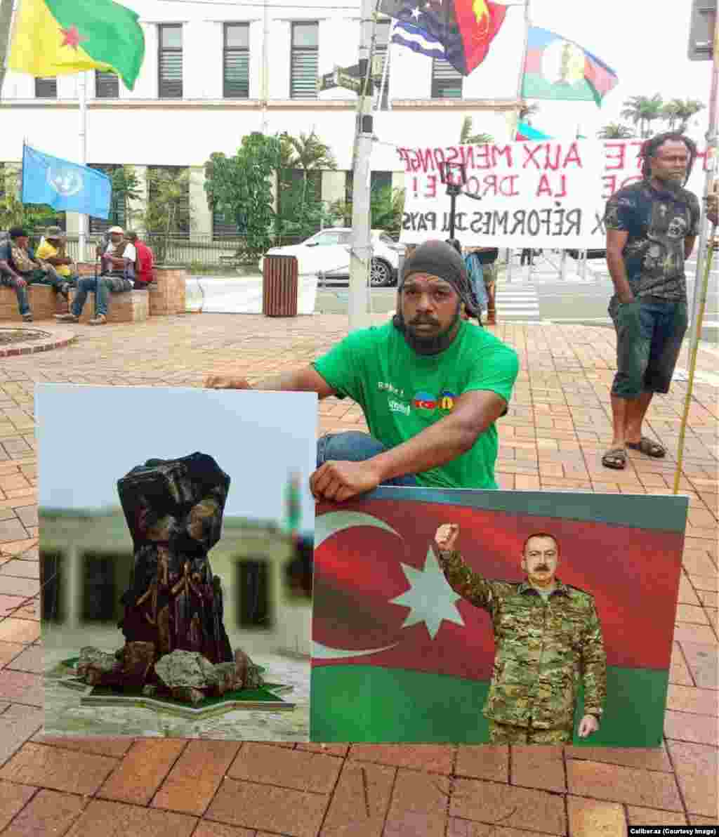 A protester in Noumea is photographed in March holding pictures of Azerbaijani President Ilham Aliyev and of an Azerbaijani war memorial. The pictured memorial was recently unveiled in Azerbaijan's retaken Kalbacar district.  