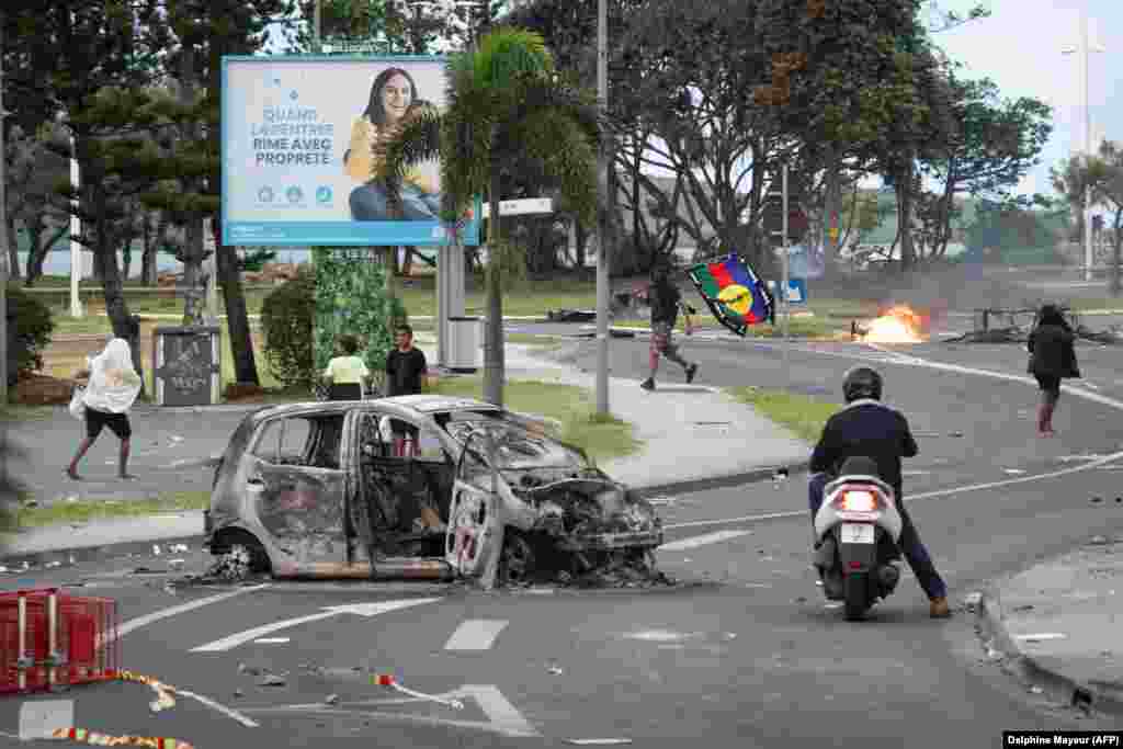 People, including a man carrying a Kanak flag, are seen as a nearby supermarket was looted in Noumea on May 14. The current unrest broke out after Paris changed New Caledonia’s constitution to allow people who have lived in the territory for 10 years or more to vote. Kanak leaders have accused Paris of seeking to dilute the democratic power of the indigenous population.   