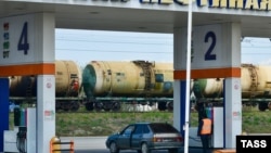 Заправка автомобиля на автозаправочной станции «Южной нефтяной компании». На дальнем плане - железнодорожные цистерны для транспортировки нефтепродуктов. Россия, Краснодар, 2020 год. Иллюстрационное фото