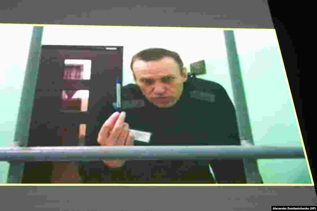 Лидер российской оппозиции Алексей Навальный на экране телевизора по видеосвязи, предоставленной ФСИН России из колонии в Мелехово Владимирской области, во время слушаний в Верховном суде России в Москве. Россия, 22 июня. Навальный подал иск, оспаривая тюремные правила, которые, по его словам, позволяют тюремным чиновникам лишать его канцелярских принадлежностей и ручек, тем самым нарушая его право подавать на них жалобы. (AP Photo/Alexander Zemlianichenko)