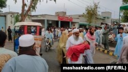 د بنو اوسېدونکي د روغتون د بیړنیو روغتیايي خدماتو څانګې مخې ته ولاړ دي او یو تن یوه ژوبله ماشومه تر درملنې وروسته کور ته لېږدوي - د جون ۱۰مې انځور.