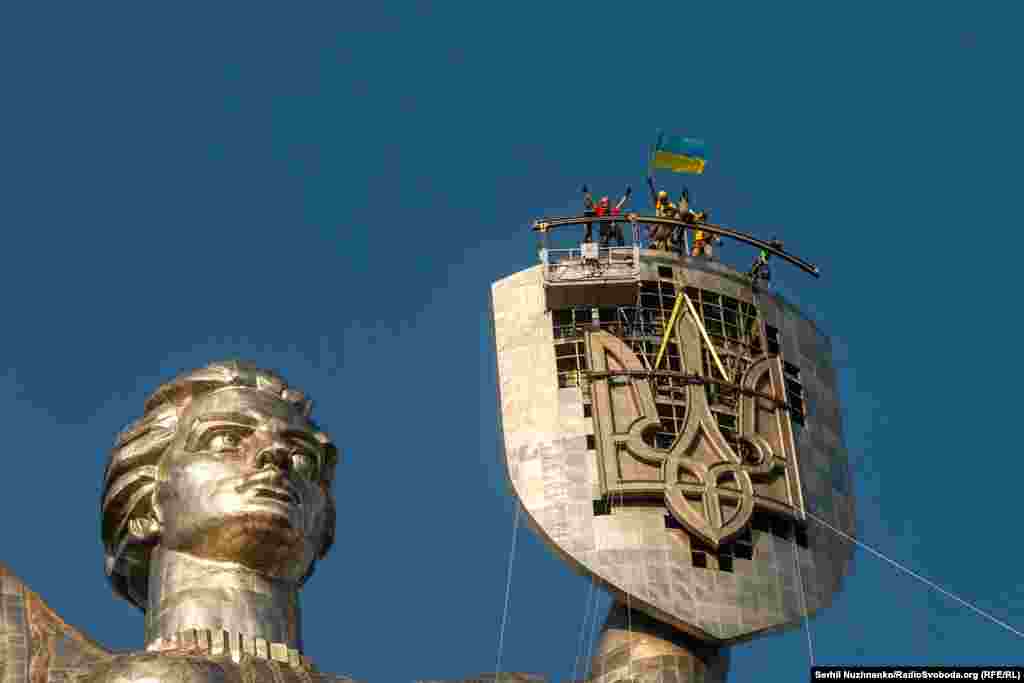 Workers celebrate after the installation of the Ukrainian trident on the shield of Kyiv's motherland monument on August 6, 2023. The massive trident replaced a Soviet emblem. 