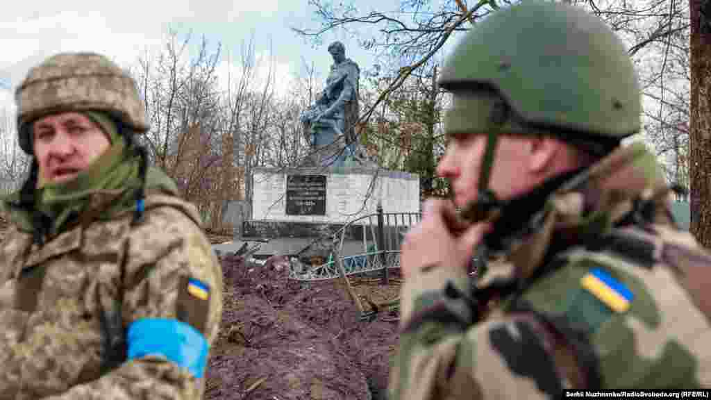Українські військовослужбовці стоять біля пошкодженого меморіалу загиблим воїнам у Другій світовій війні у нещодавно звільненому селі Лук'янівка на Київщині, 27 березня 2022 року