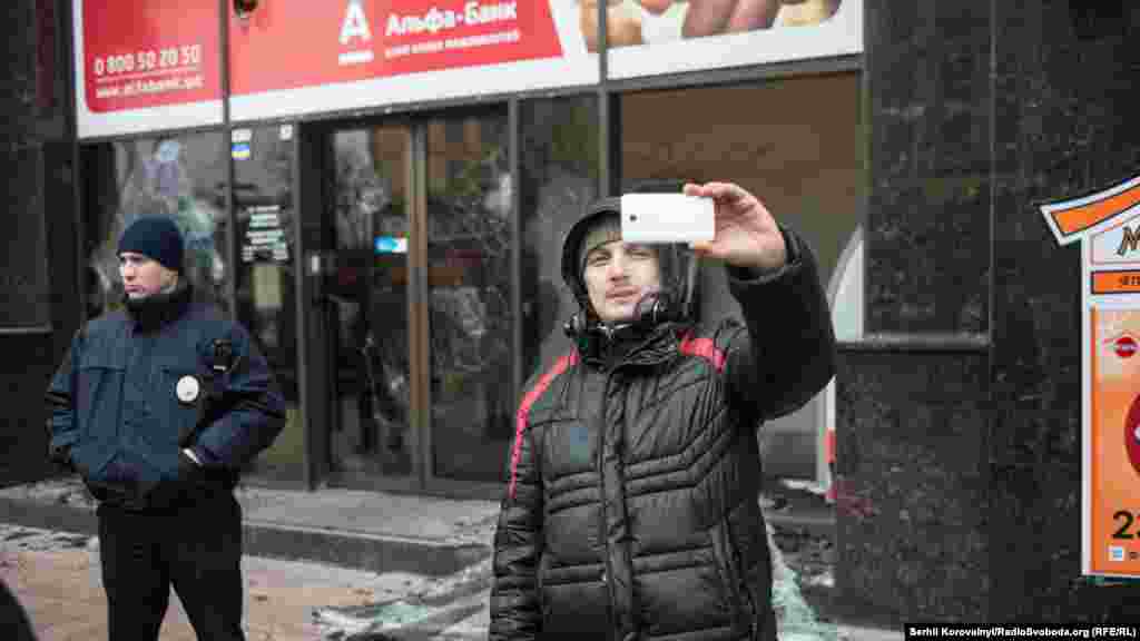 Мужчина делает Селфи на фоне «Альфа-банка». Следователи работают в разгромленном «ОУНовцами» помещении финучреждения