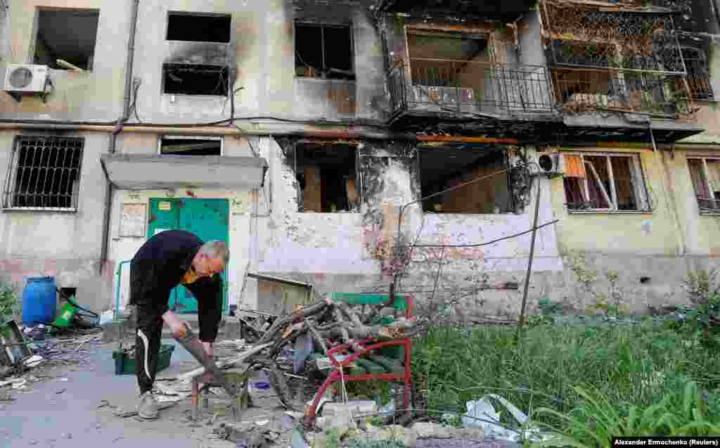 A local resident cuts firewood outside a damaged residential building on May 12. Under Russian control the city is struggling to restore basic services such as electricity and water.