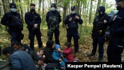 An Iraqi migrant woman with children sits on the ground as they are surrounded by Polish border guards and police officers in Hajnowka after crossing into Poland from Belarus.