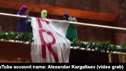 A screen grab from a video of three masked women wearing customary "Pussy Riot" balaclavas and unfurling a large banner with the slogan "Free Sentsov" inside Trump Tower in New York on October 24.