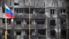 Российский флаг на фоне разрушенного в ходе войны здания в Мариуполе