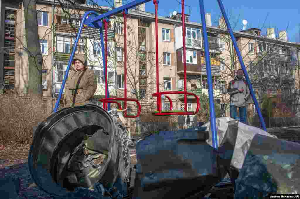 Пас аз ҳамлаи ҳавоии Русия дар Харков, як мард ва як зан дар паҳлӯи таҷҳизоти низомӣ истодаанд.    