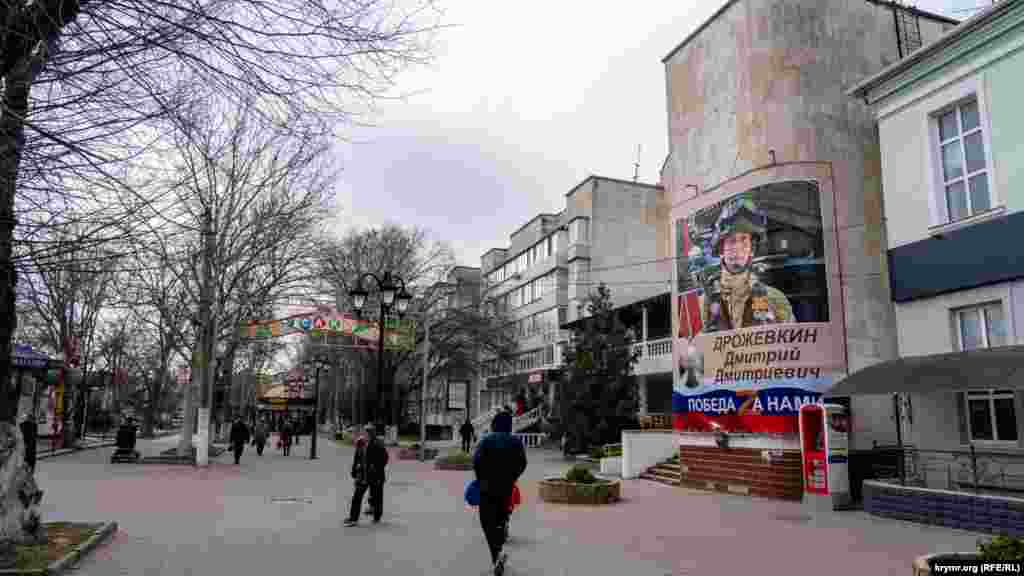 На площадь Революции с запада выходит улица Революции, где в прошлом году повесили большой баннер с фото умершего в военном госпитале в результате минометного ранения в ходе «СВО» старшего сержанта Черноморского флота РФ Дмитрия Дрожевкина. Мемориальную доску с его изображением тогда же повесили и на фасаде его пятиэтажке в соседнем поселке Новофедоровка