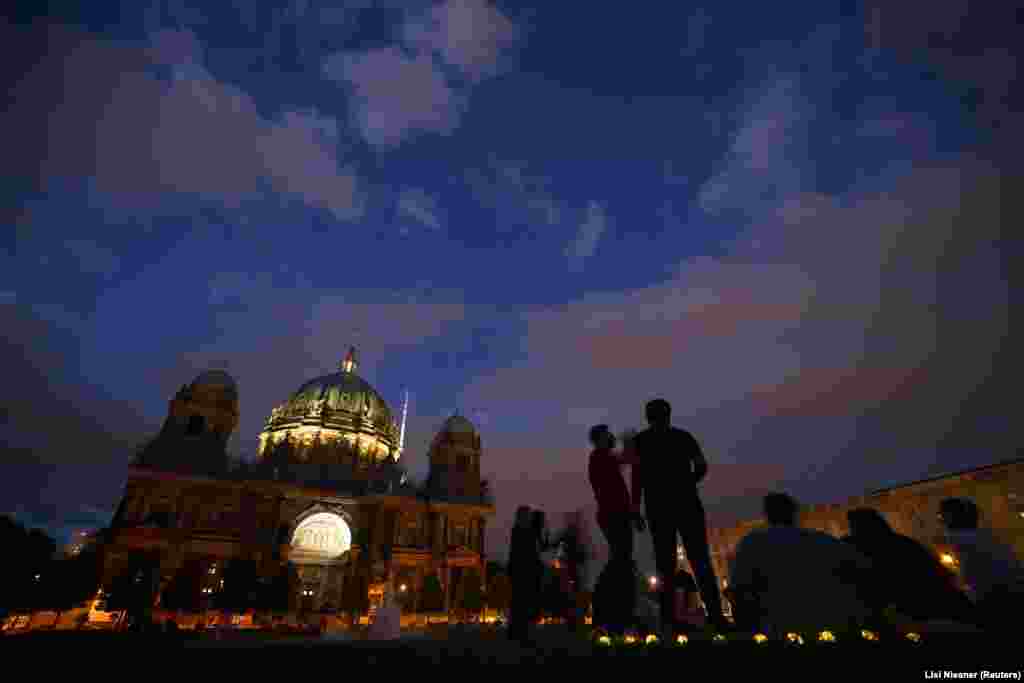 In Berlin too, historic sites stand largely unlit after sunset. People enjoy a summer evening next to Berlin's central cathedral.   