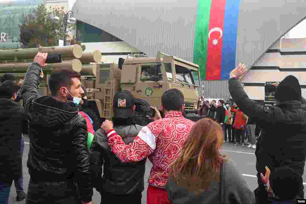 Зрители машут руками и снимают видео, когда мимо проезжает система залпового огня Т-300 «Касирга» турецкого производства