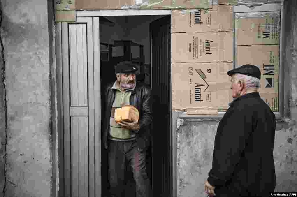 A man emerges from the bakery with fresh loaves of bread.  