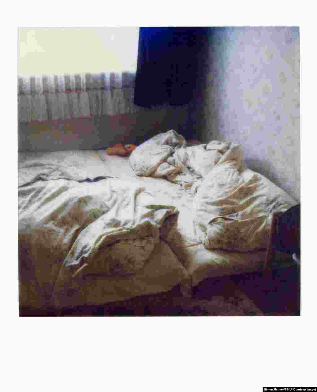 Поляроидная фотография кровати в пустой квартире. Такие фотографии часто делались во время проведения тайных обысков, чтобы агенты Штази могли оставить вещи после ухода в том же состоянии, в котором их оставил ничего не подозревающий жилец квартиры.  