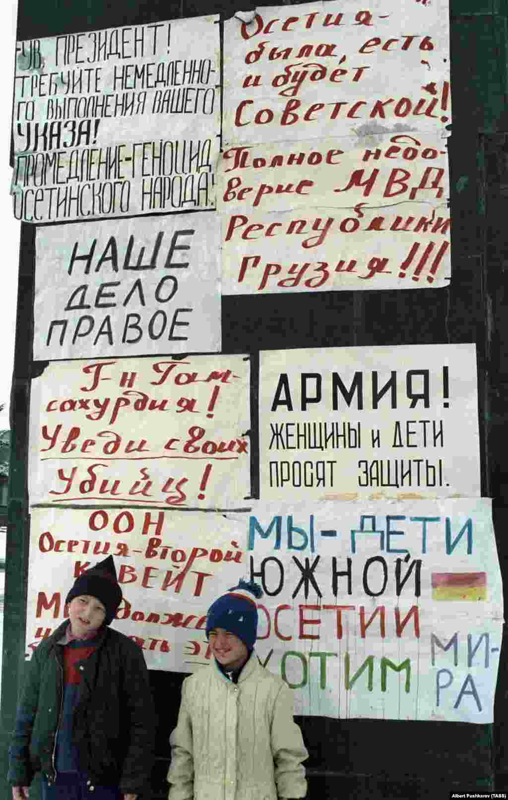 Дети в Цхинвали 1 января 1991 года позируют рядом с плакатами на памятнике Ленину, который осетины не позволили снести. На одном из плакатов написано: «Осетия была, есть и всегда будет советской». Многие грузины считали этнических осетин предательской «пятой колонной» в то время, как их страна боролась за свободу от Советского Союза. А осетины чувствовали себя отстраненными от новых законов, которые сделали грузинский язык единственным официальным языком страны и препятствовали политическому представительству осетин в Тбилиси  