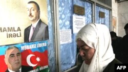 A woman stands near election posters for current Azerbaijani President Ilham Aliyev