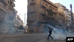 A protester throws a tear gas bomb back towards security forces in the flashpoint city of Homs.