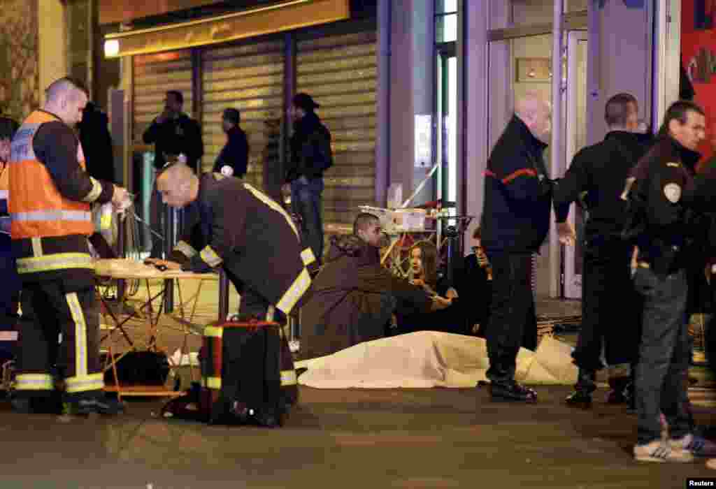 A French rescue worker checks his laptop computer as three people consol each other over the body of a shooting victim. 