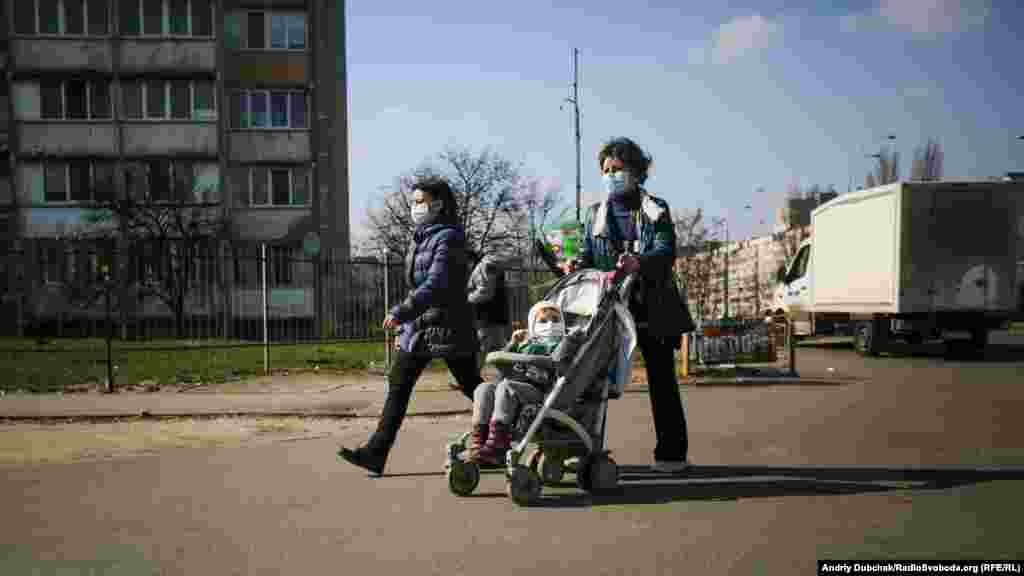 Женщины с ребенком в медицинских масках идут по улице возле метро «Героев Дпепра». Карантин в Украине продлится минимум до 3 апреля 2020 года
