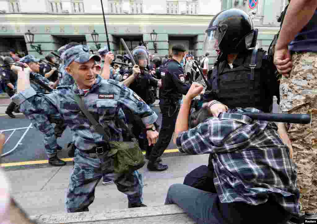 A Russian national guardsman beats a protester with a rubber baton during protests in Moscow. Video of the incident show the guardsman striking the detained man twice with full force, before a bystander punches the riot policeman on right. 