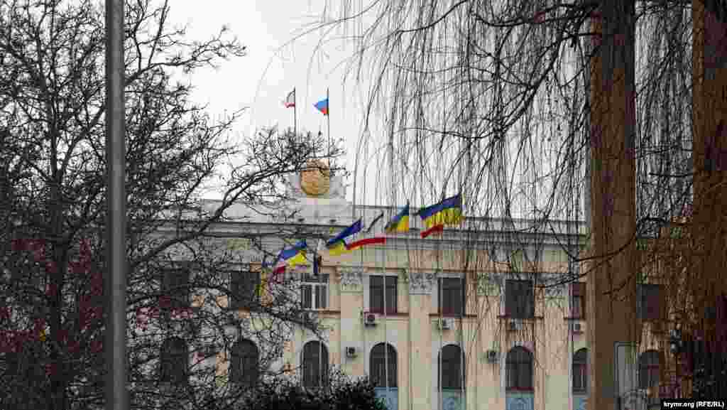 Последние украинские флаги в городе. «Ополченцы» бы их давно сорвали, но флагштоки стоят перед зданием Совета министров, в зоне оцепления, куда не пускает милиция. А «зеленые человечки» пока из Совмина и Верховной Рады так и не выглянули. В этот день, в пятницу,  администрация школ в центре Симферополя  рекомендовала школьникам пропустить занятия. Не приказала, а именно рекомендовала Это был последний день зимы 2014 года.