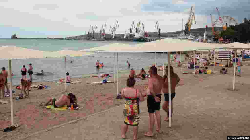 Туристы пытаются поймать редкие лучи солнца на пляже у порта 