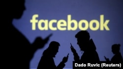 Silhouettes of mobile users are seen next to a screen projection of Facebook