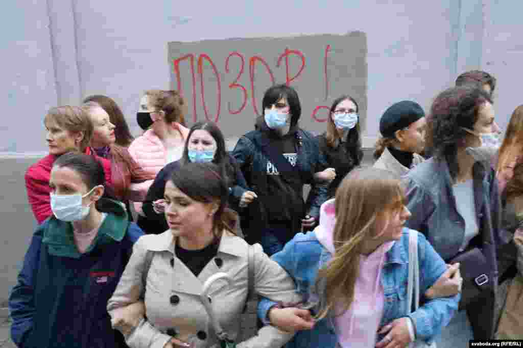 Protesters link arms in front of a wall where the word "SHAME!" has been written. 