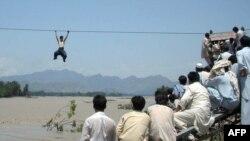 Onlookers perched on a damaged bridge watch a Pakistani flood survivor climb a rope to cross a river in Pakistan's Swat Valley on August 3.