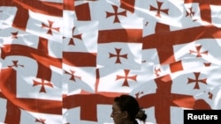 A woman walks past a wall decorated with Georgia's national flags in the center of Tbilisi.