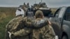 A Ukrainian soldier helps a wounded member of his unit on the road in Ukraine's Kharkiv region in 2022.