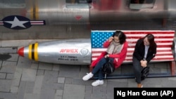 Китайские женщины сидят на скамейке с флагом США у магазина одежды в Пекине