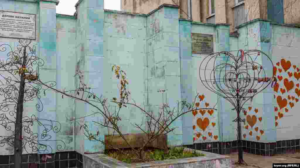 «В гнездо монетку брось – семья не будет врозь» написано на табличке над кованым «деревом желаний». Справа от него – «дерево любви и счастья»