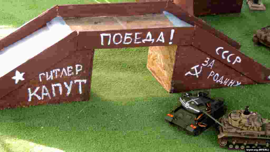 На іграшкових танках зав'язані георгіївські стрічки, написи на атракціоні говорять: «Гітлер капут», «СРСР», «Перемога!», «За Батьківщину»