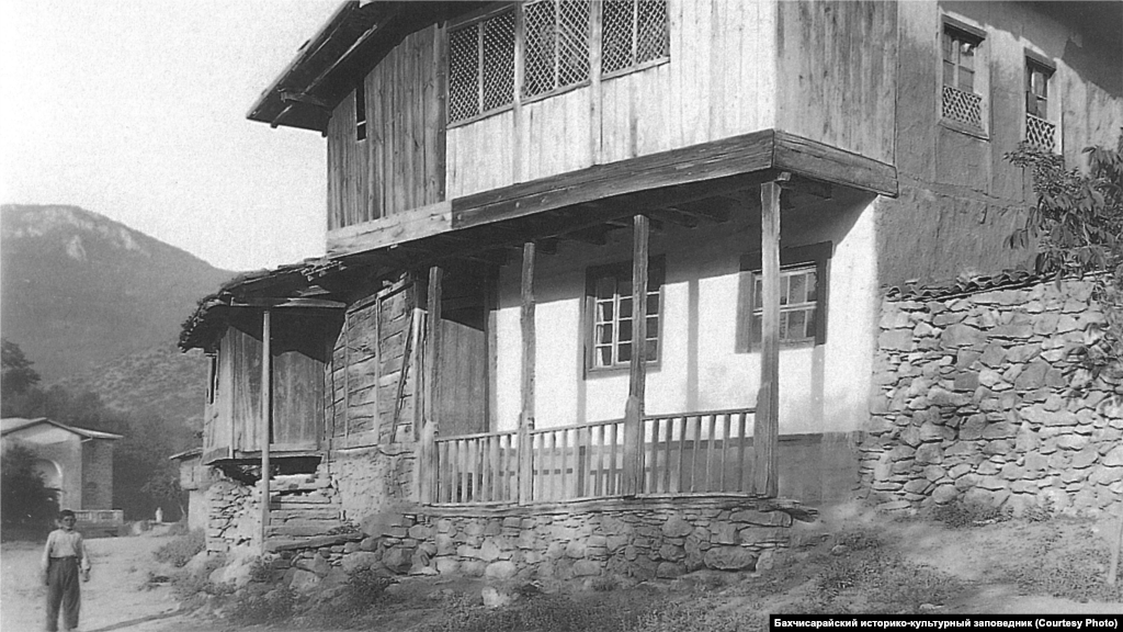 Сельский дом. Юго-Западный Крым, 1920-ые. Стандартный интерьер главной комнаты включал открытый камин с дымоходом и подвешенный к нему на цепи казан. Вдоль стен стояли низкие диванчики с матрацами и подушками, рядом – столики. Для украшения стен использовались многочисленные полотенца, а для пола – ковры