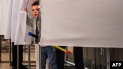 A young boy peeps out from behind the curtains of a voting booth at a polling station during the municipal elections in Moscow on September 10.
